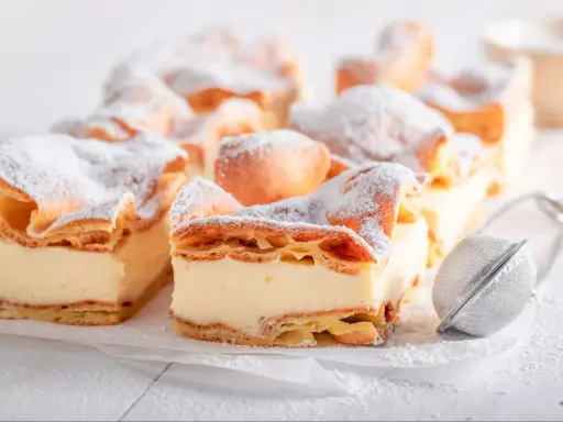 Kremówka papieska, jeden z 10 najlepszych ciast, posypana cukrem pudrem.