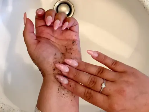 Manos con uñas largas y rosadas, cubiertas de gránulos oscuros. Parece un autobronceador mal aplicado que se está intentando lavar.