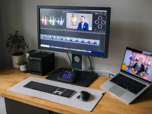 Stacja do edycji wideo z monitorem BenQ, laptopem, klawiaturą i kontrolerem. Na ekranie widać oś czasu i wykresy, co sugeruje pracę nad parametrami monitora.