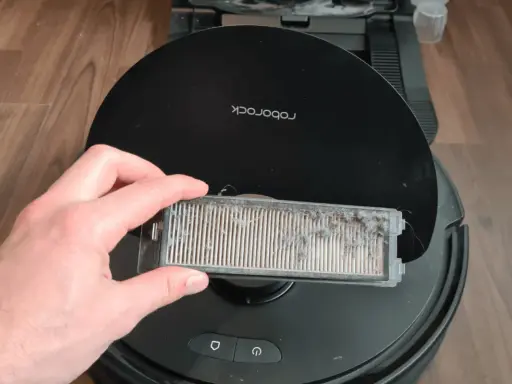 Hand hält einen stark verschmutzten Staubfilter eines Roborock Saugroboters, bereit für die Reinigung.