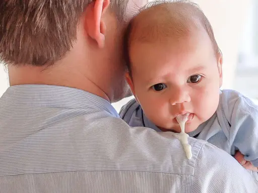 Un padre tiene in braccio il suo neonato, che ha un rigurgito visibile.
