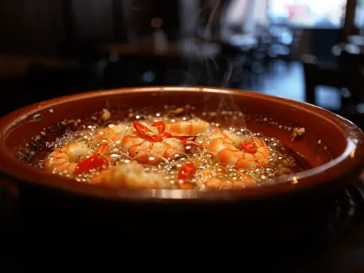 Gambas al ajillo burbujeantes en cazuela de barro, con guindillas rojas y vapor ascendiendo.