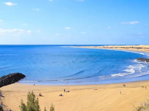 Sonniger Strand auf Gran Canaria mit goldenem Sand, türkisfarbenem Meer und einigen Menschen, die die Sonne genießen.