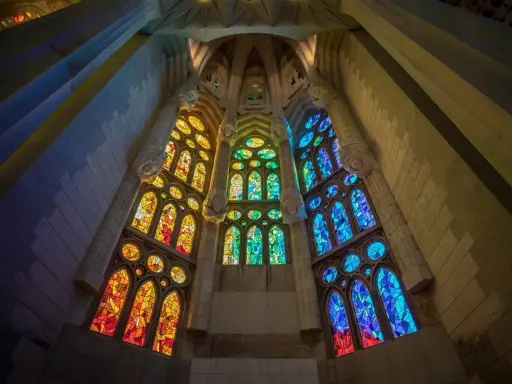 Ventanas de vidrieras de colores vibrantes, que narran la historia del vidrio, iluminan el interior de una catedral con tonos cálidos y fríos.