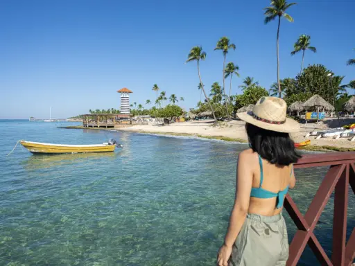 Kobieta w kapeluszu podziwia plażę z latarnią i palmami. Czy to Puerto Plata czy Punta Cana?