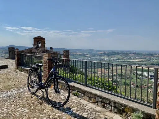 Bicicletta pronta per esplorare il **percorso fiume Marecchia**, con vista panoramica sulla valle e un antico campanile.