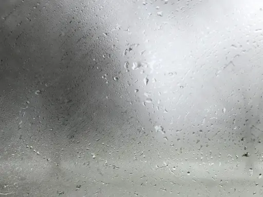 Gotas de agua sobre un cristal, reflejando un cielo nublado. La **temperatura de rocío** se siente en el aire húmedo.