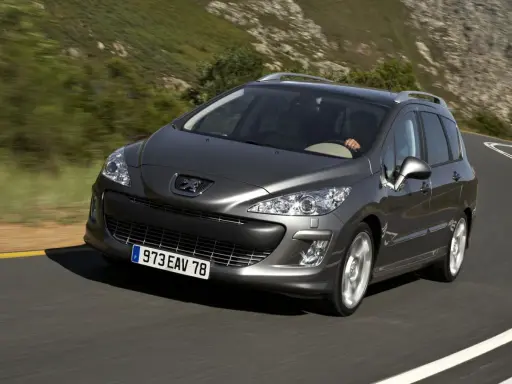 Szary Peugeot 308 2008 na krętej drodze wśród zielonych wzgórz.