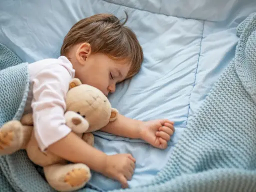 Małe dziecko śpi z misiem. Nadmierna senność u niemowlaka może mieć różne przyczyny, ale ten maluch wygląda na spokojnego.