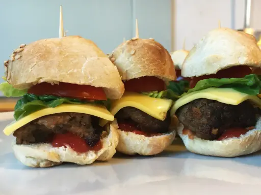 Drei leckere Slider Burger mit Käse, Tomate und Salat auf einem Teller.