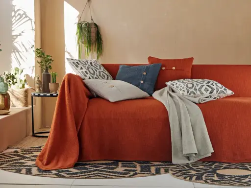Un canapé ancien relooké en orange vif, orné de coussins graphiques et d'une couverture grise. Une touche bohème moderne.
