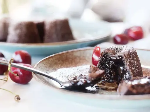 Coulant de chocolate con interior fundido, espolvoreado con azúcar glas y acompañado de cerezas frescas.