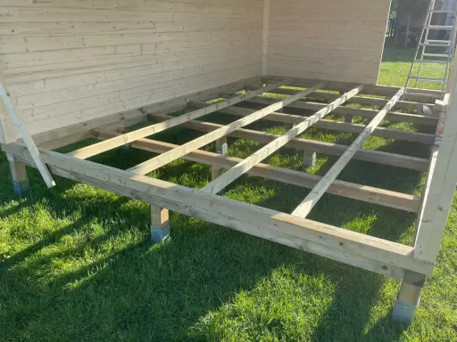 Holzkonstruktion für das Gartenhaus. Der Boden wird auf Balken und Pfosten errichtet, die auf dem Rasen stehen.