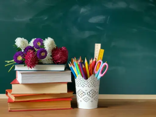 Kwiaty na stosie książek i przybory szkolne na tle zielonej tablicy. Idealna kompozycja na Dzień Edukacji Narodowej.