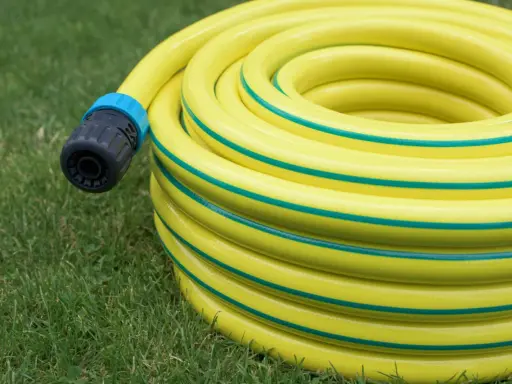 Un tuyau d'arrosage jaune enroulé sur l'herbe, avec un connecteur noir et bleu. Le diamètre du tuyau d'arrosage est visible dans son enroulement.