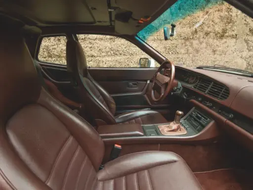 Das **Porsche 944 Interieur** mit braunen Ledersitzen und Armaturenbrett. Ein Blick auf das Lenkrad, den Schalthebel und das Radio.