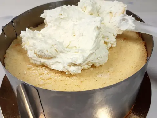 Nakładanie puszystego kremu mascarpone na biszkopt w tortownicy.