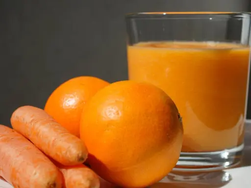 Pomarańcze i marchewki obok szklanki soku. Idealne składniki na zdrową dieta warzywno owocowa.