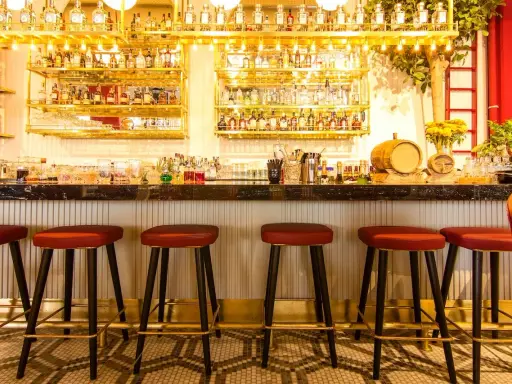 Bar con botellas doradas y taburetes rojos. Ideas para decorar un bar con poco dinero: ¡la iluminación y los detalles marcan la diferencia!