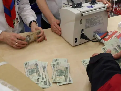 Ręce liczą banknoty 100 i 200 zł. Obok maszyna do liczenia pieniędzy. W tle gazety. Płatność gotówką do jakiej kwoty jest dozwolona?