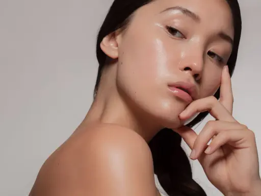 Młoda kobieta z idealną, lśniącą cerą typu "glass skin", delikatnie dotykająca twarzy.