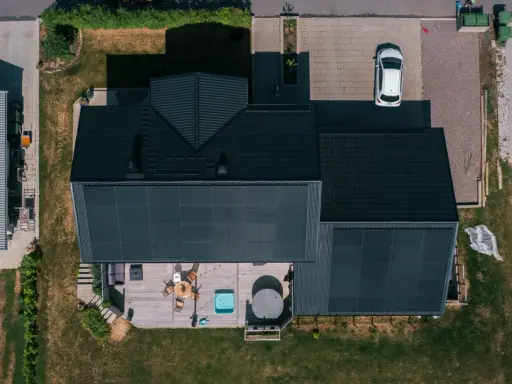 Villa med solceller och ett modernt batterilager. Uteplats med spabad och utemöbler. En vit bil parkerad på uppfarten.
