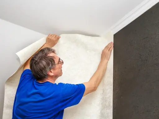 Hombre colocando papel tapiz texturizado, un paso para insonorizar habitación y mejorar la acústica.