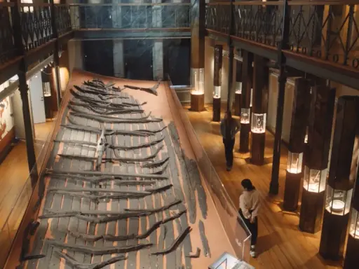 Vikingaskeppsvrak på ett museum i Göteborg. Besökare studerar utställningen med gamla trädelar.