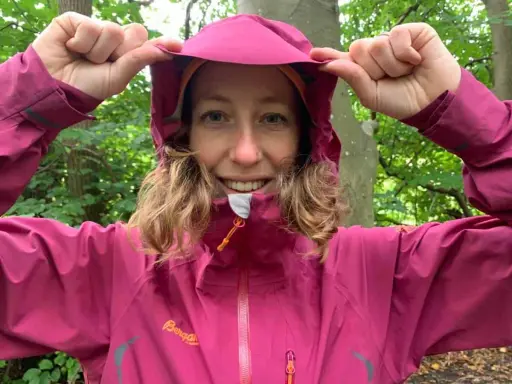 Kvinna i skogen drar upp huvan på sin rosa jacka, redo för 5000 vattenpelare.