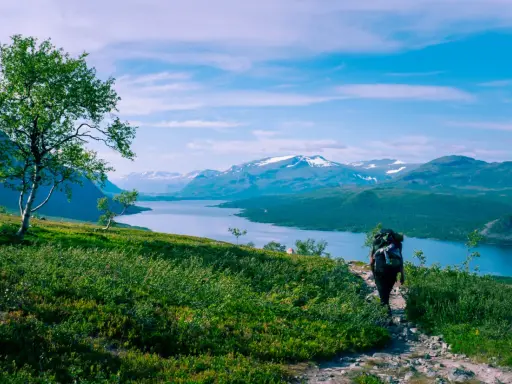 Vandra i Norrland med storslagen utsikt över sjö och snöklädda berg. En ensam vandrare med ryggsäck går på en stenstig.