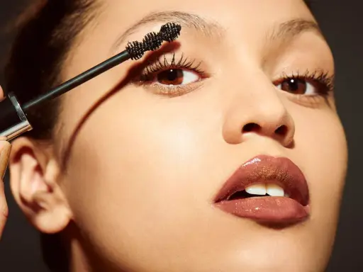 Una mano aplica máscara de pestañas a unos ojos pequeños, resaltando su belleza natural.