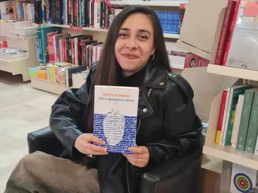 Una giovane donna sorride in libreria, tenendo in mano il libro "Dove si nascondono le lacrime".