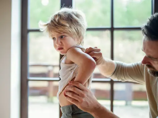 Un père examine le dos de son enfant, peut-être pour vérifier une poussée d'eczéma.