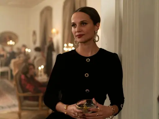 Alicia Vikander i en elegant svart klänning med stora örhängen, håller ett glas. Scenen utspelar sig på en tillställning, kanske från en av hennes filmer.