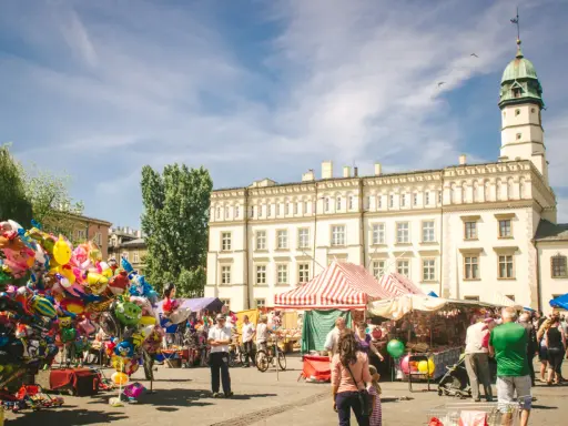 Kolorowy jarmark na rynku na Kazimierzu w Krakowie. Balony, stragany z pamiątkami i ludzie spacerujący pod jasnym niebem.