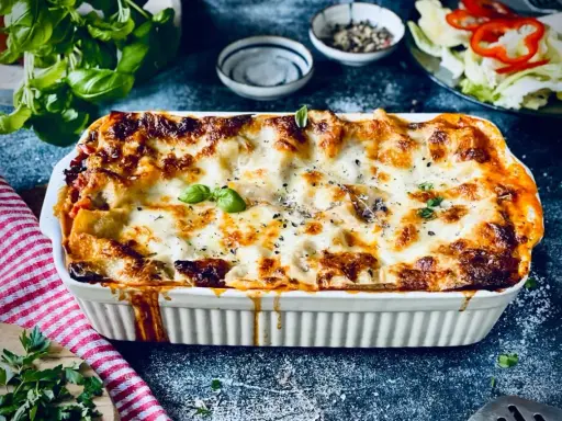 Herzhafte vegetarische Lasagne mit geschmolzenem Käse und frischem Basilikum, serviert in einer weißen Auflaufform.