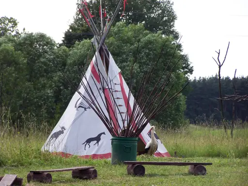 Wioska indiańska na Mazurach z tipi ozdobionym zwierzętami, bocianem i łukami.