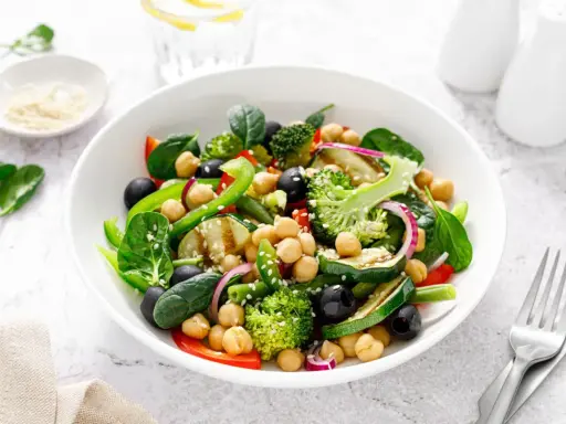 Ensalada de legumbres vibrante con garbanzos, brócoli, espinacas, aceitunas negras y pimientos verdes.