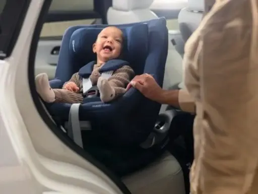 Bebé sonriente en un maxicosi azul, listo para aprender como colocar el maxicosi en el coche.