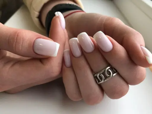 Dłonie z idealnym french manicure. Paznokcie prostokątne w delikatnym różu z białymi końcówkami, ozdobione srebrnym pierścionkiem.