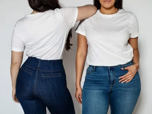 Dwie kobiety w białych T-shirtach i jeansach. Jedna ma na sobie ciemne jeansy z wysokim stanem, podkreślające szerokie biodra stylizacje.