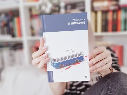Dłonie trzymają książkę "Nie oświadczam się" z okładką przedstawiającą niebieski autobus i plamy krwi.