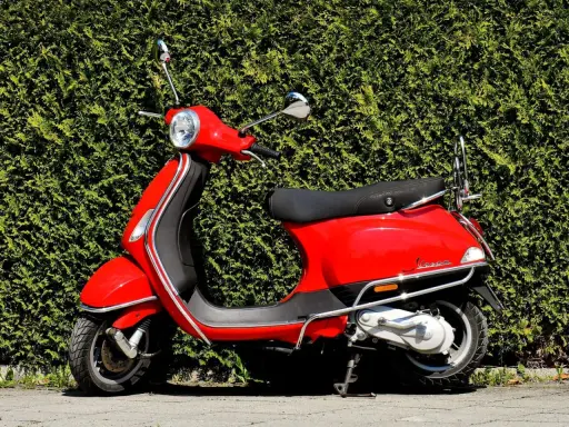 Scooter rojo brillante aparcado frente a un seto verde. ¡Listo para salir con mi permiso AM!