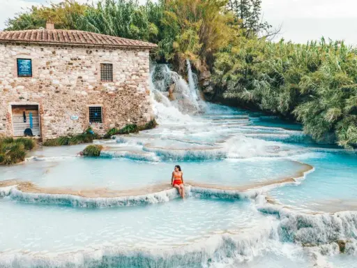 Cascate naturali con acqua turchese, una donna seduta su una roccia. Un antico mulino in pietra sullo sfondo. Tra le terme più belle d'Italia.