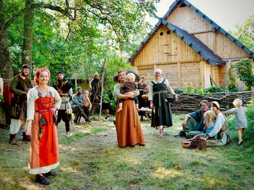 En grupp människor i vikingakläder samlas framför ett trädhus i vikingabyn Storholmen.