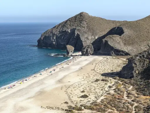 Sonnige Playa de los Muertos mit türkisfarbenem Meer, Felsen und vielen Sonnenanbetern.