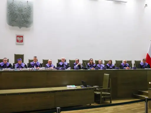 Sędziowie w togach siedzą za stołem w sali sądowej, przygotowując się do rozprawy przed trybunałem stanu.
