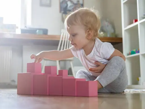 Bambina bionda gioca con blocchi rosa, ideali come giochi montessori 6 mesi fai da te per sviluppare la coordinazione.