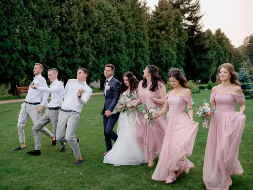 Para ślubna z drużbami i druhnami w eleganckim ubiorze na ślub, idący przez trawnik.