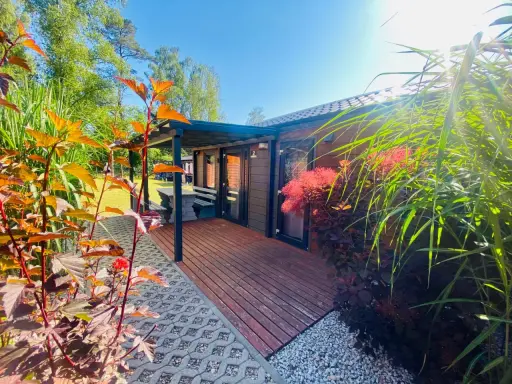 Uroczy tiny house wynajem. Drewniany domek z tarasem, otoczony zielenią i kwitnącymi krzewami. Idealne miejsce na relaks.